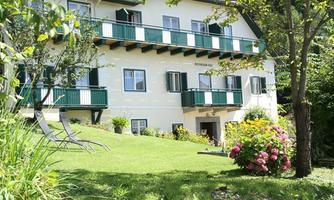 A beautiful house with a green balcony and shutters. The garden is blooming and inviting with colorful flowers and lawns.
