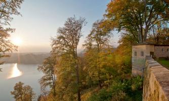 A picturesque landscape with a tranquil lake and colorful autumn trees. The sun rises on the horizon, casting warm light over the scene.