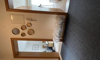 A modern entrance area with a rug and a cushioned seat. Round mirrors hang on the wall, and the room leads to a bright living area.