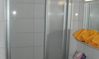 A simple bathroom with a shower cubicle, a sink, and a mirror. Yellow towels are hanging on the wall.
