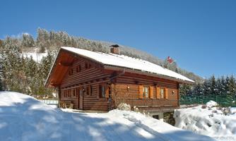 A beautiful wooden house in winter, surrounded by snow. The clear blue sky completes the winter landscape.