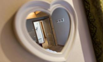 A heart-shaped mirror reflects a cozy room with a wooden door. Subtle decorative elements are visible in the background.
