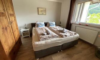 A cozy bedroom with a large bed and wooden wardrobes. The window offers a view of the greenery.