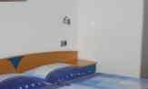 A simple bedroom with a double bed and blue blankets. Some pictures are hanging on the wall.