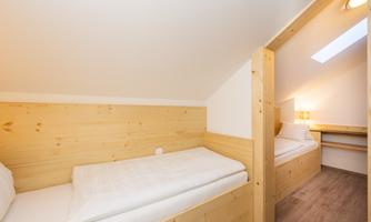 A simple bedroom with two wooden single beds. The room has a cozy atmosphere and a window that lets in natural light.
