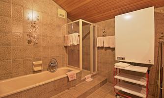 A modern bathroom with a shower and a bathtub. The walls are tiled in neutral colors, and there are towels and a small cart for utensils.