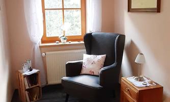 A cozy room with an armchair and a small table. The window lets in a lot of natural light and the walls are painted in a light color.