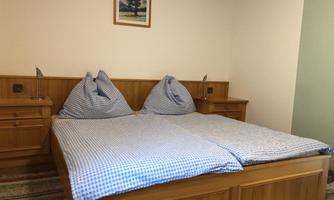 A cozy room with a double bed and checked bedspreads. A picture of a tree hangs on the wall.
