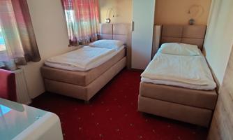 A simply furnished room with two single beds. There is a table and a chair, as well as bright curtains.
