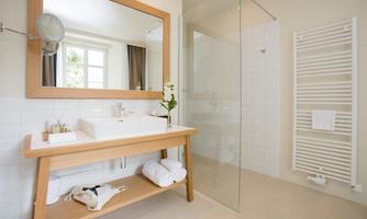A modern bathroom with a large mirror and an elegant shower. Towels and toiletries are arranged on a wooden table.