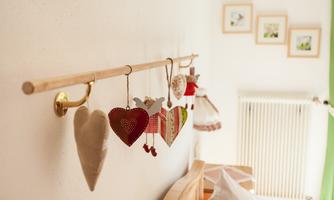 A decorative rod with hanging little hearts made of fabric and wood. In the background, a radiator and picture frames on the wall are visible.