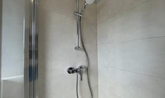 A modern shower with a simple, bright tiled wall. The showerhead is elegant and functional.