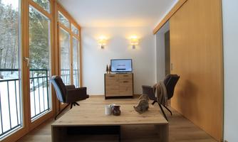 A modern living room with large windows that provides plenty of daylight. Two comfortable chairs and a wooden table create an inviting atmosphere.