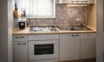 A modern kitchen with a stove, a sink, and a refrigerator. The room is bright and equipped with a window blind.