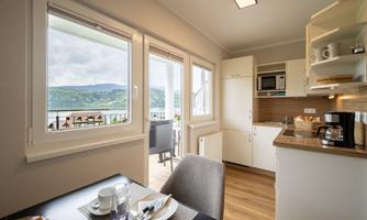 A bright, modern kitchen with a view of the lake. The table is set and there is fresh fruit.