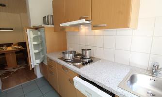 A modern kitchen with wood cabinets and a stove. In the background, a dining table is visible.