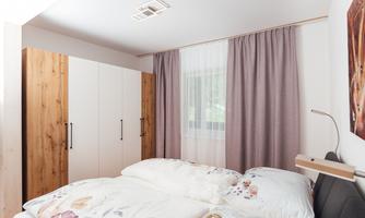A modern bedroom with a double bed and blooming bedding. Against the wall, there is a bright wardrobe and curtains in soft colors.
