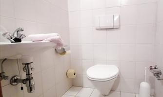 A simple, clean bathroom with white tiles. There is a sink, a toilet, and basic plumbing fixtures.