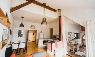A bright and modern apartment with open spaces and wooden beams. The cozy furnishings include a living area, a kitchenette, and dining spots.