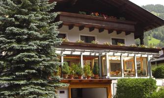 A cozy house with a large glazed winter garden and a well-maintained garden. In the foreground, there is a large tree that provides shade.