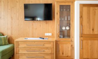 A cozy living area with wooden panels and a television on the wall. Next to the TV is a sideboard with a glass showcase and a green couch.