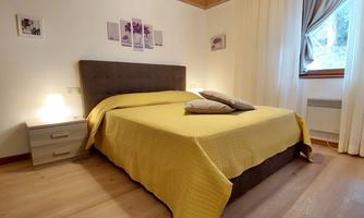 A cozy bedroom with a large bed and a yellow duvet. Natural light falls through the window, creating a warm atmosphere.