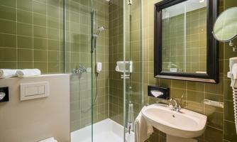 A modern bathroom with a glass shower and green tiles. Next to the sink are towels and a large mirror.