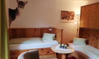 A cozy room with two single beds and wooden furniture. On the wall, there is a picture of a doe, giving the room a natural atmosphere.