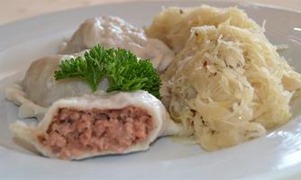 A plate with filled dumplings and sauerkraut. The dumplings are filled with meat and garnished with a little parsley.