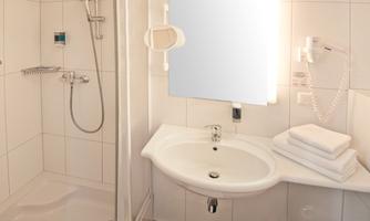 A modern bathroom with a shower, sink, and mirror. The walls are tiled in white and the decor is simple and functional.