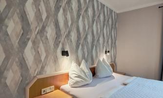 A comfortable bedroom with a double bed and cozy pillows. The walls are decorated with a modern, geometric pattern.
