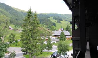 A picturesque landscape with green hills and sparsely populated houses. Tall trees surround the scene, conveying a calm, natural atmosphere.