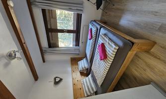 A simple room with two single beds and striped bedcovers. The windows are equipped with curtains and the floor is wooden.