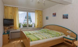 A cozy bedroom with a large bed and colorful bedspreads. The room has a television and bright curtains that let in light.