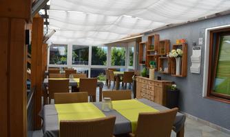 A bright and inviting restaurant with wooden furniture. The tables are decorated with green tablecloths, and there is a large window front.