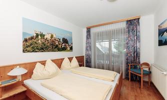 A bright room with two beds and a large window.  
On the wall hangs a picture of a castle on a hill.