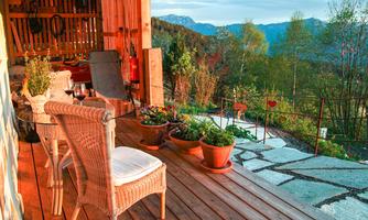 A cozy terrace with chairs and pots full of plants. Mountains and trees are visible in the background.