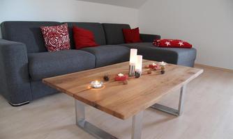 A modern living room with a gray sofa and red pillows. In the center stands a wooden table with candles and decorations.