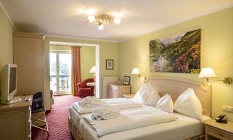 A cozy hotel room with two beds, a television, and a window with a view. The walls are painted in light colors and a picture of a landscape hangs on the wall.