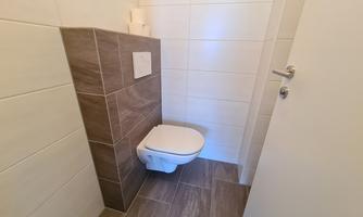 A modern bathroom with a toilet and elegant tiles. The walls are tiled in light colors, and the floor has a natural stone look.