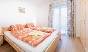 A cozy bedroom with two single beds and colorful blankets. Large windows let in plenty of daylight.
