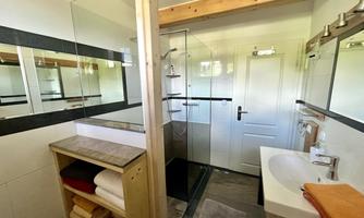 A modern bathroom with a shower and a sink. Wooden shelves with towels and large mirrors complement the design.