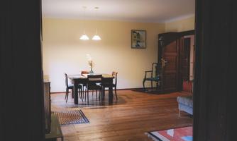 A bright dining room with a wooden table and chairs. The floor is made of wood and there is a cozy atmosphere.