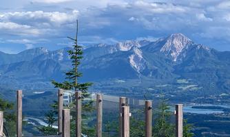 An impressive mountain landscape with high peaks and a clear view. In the foreground, there are wooden posts and trees.