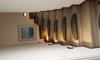 A bright staircase with round handrails leads upwards. There are modern light sources on the walls.
