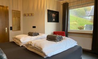 A cozy bedroom with two beds and fresh blankets. A window offers a view of the green landscape outside.