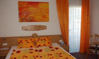 A bright bedroom with orange curtains and bedding. A colorful piece of artwork hangs on the wall.