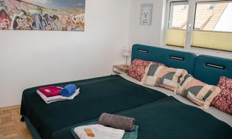 A cozy bedroom with two beds and colorful cushions. There are bright curtains at the window and a graffiti painting on the wall.