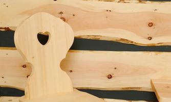 A handcrafted wooden chair with a heart-shaped cutout. The chair is situated in front of a rustic wooden wall.