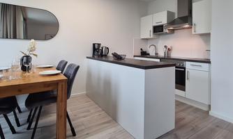 Modern kitchen with white cabinets and a cooking island. A dining area is furnished with a wooden table and chairs.